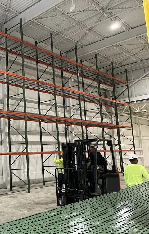 Tall pallet racking going up in a bright warehouse, with an installer and a forklift on the floor
