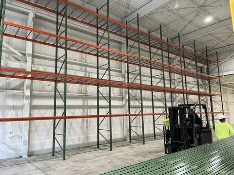 Tall pallet racking going up in a bright warehouse, with an installer and a forklift on the floor